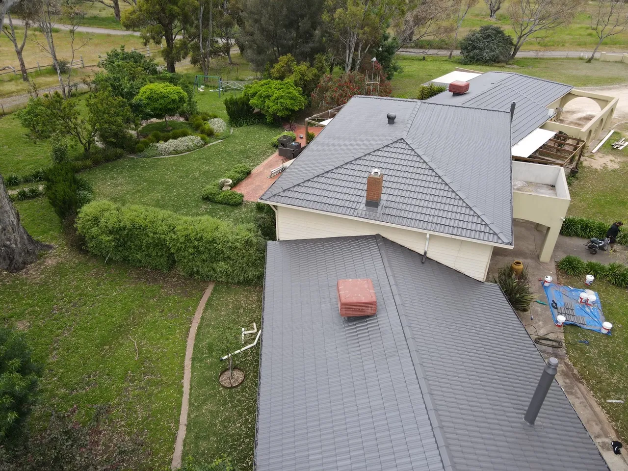 Tile roof freshly painted in charcoal grey, with the paint gear still laid out on a tarp beside the house, roof painting in the Bendigo region