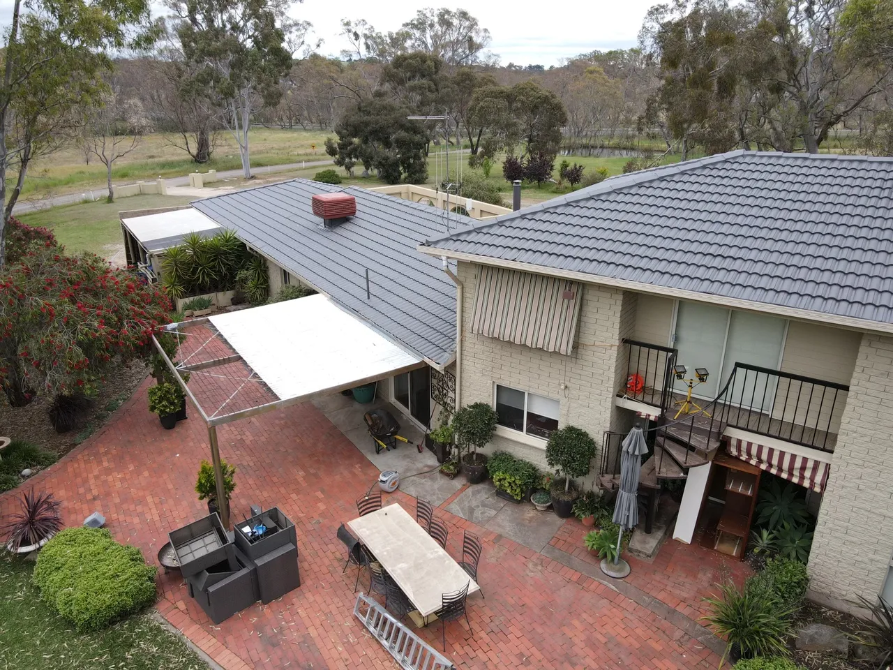 Over the courtyard Restored charcoal tile roof on a two storey brick home above a paved courtyard and outdoor dining area, tile roof restoration by Roof Restoration Services Bendigo
