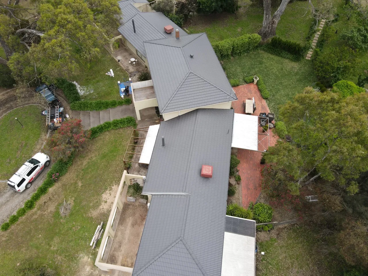 Aerial view of a full concrete tile roof restoration by JTM Roof Restorations, with the work ute and ladders beside the driveway