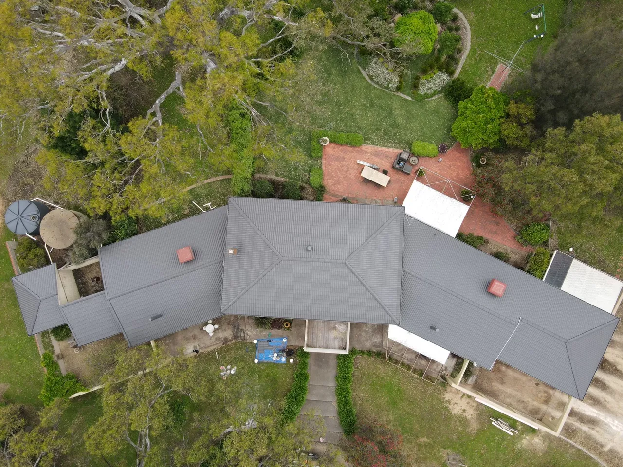 The whole roof from above Overhead drone view of a large hipped concrete tile roof, evenly recoated in charcoal grey across every wing, tile roof restoration by Roof Restoration Services Bendigo
